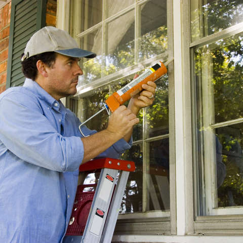 Homeowner sealing air leaks around window.